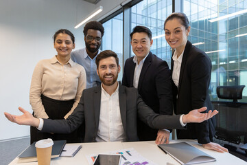 A group of professional team members smile and pose in a modern corporate environment around a desk. They exude confidence and collaboration, symbolizing teamwork, diversity, and success.