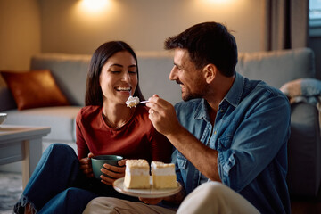 Happy man feeding his girlfriend with cake at home.