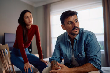 Displeased man ignoring his girlfriend after their argument at home.
