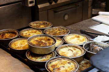 Part of a restaurant kitchen with a tray full of small round pans with already baked pies