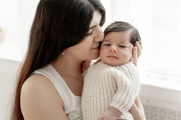 a mother holds a baby in her arms, admiring and kissing it, the birth of a baby, parental love and care, mother and baby