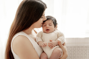 a mother holds a baby in her arms, admiring and kissing it, the birth of a baby, parental love and care, mother and baby