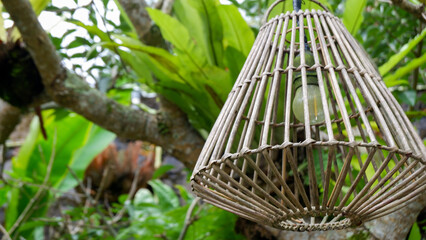 Close up of a woven rattan pendant lights with green plant bacground. A lampshade woven from rattan. A hanging lamp for outdoor use, home gardens, restaurants and decoration of a room's. interior. 