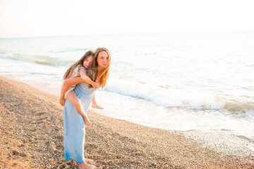 Happy mother holding kid girl daughter 5-6 year old walking at beach over sea background outdoors. Motherhood. Summer season.