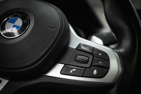 Detailed view of a BMW steering wheel featuring black leather, visible stitching, and control buttons for mode, volume, and phone connectivity.
