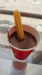 Traditional Spanish churro dipped into a thick cup of hot chocolate served in a red paper cup