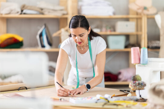 Adult female seamstress drawing pattern on paper in sewing workshop