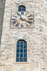 Historic clock tower on Girona Cathedral with Roman numeral clockface and arched windows, Spain. Medieval stone masonry highlights craftsmanship. Prominent timepiece on weathered limestone facade