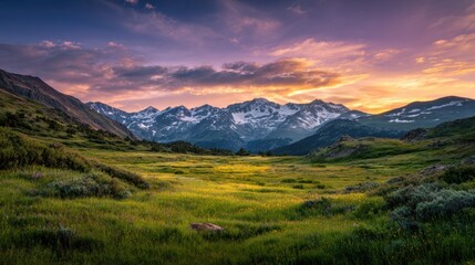 Fototapeta premium Breathtaking view of a lush green valley surrounded by majestic mountains under a vibrant sunset sky.