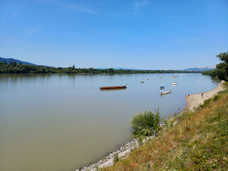 Tranquil Summer Day at a Riverside Beach with Boats and Hills