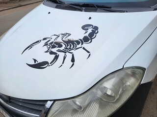 There's a black scorpion sticker on the hood of a white car.