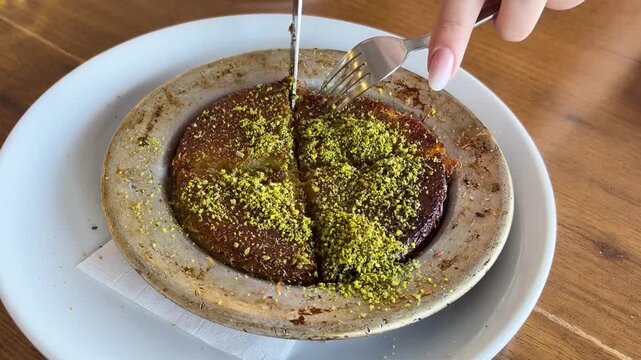 The cutting and serving of hot k&uuml;nefe decorated with pistachios reflects the unique dessert culture of Turkish cuisine.