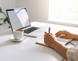 POV of a professional writing in a notebook with a pen, laptop on the side, modern workspace for returning to work, focused and organized office environment