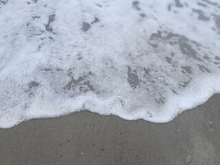 Close-up of White Sea Foam on Gray Sand as Waves Recede