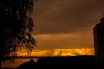 The sunset painted the sky in golden-orange hues, the sun's rays breaking through the clouds, reflecting in the calm water of the river.