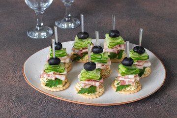 Canapes on crackers with bacon, cucumbers and black olives