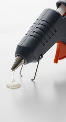 A glue gun with glue stick and drip of glue on a solid white background