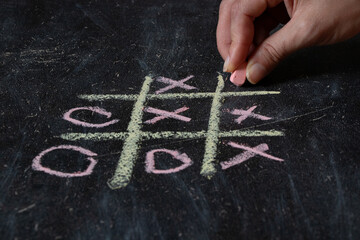 Female hand drawing tic tac toe on black school board with chalk, play