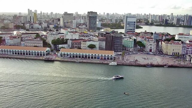 Aerial drone view of the Historic Center of Recife in Pernambuco, Brazil, showing the cityscape with Marco Zero square, the Francisco Brennand Sculpture Park area, and a boat on the water.