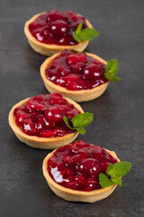 Cherry tartlets. With mint. On a wooden board. Dark background. Close up