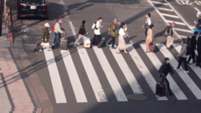 Blurred defocused of slowmotion aerial view people walking at zebra crossing in a sunset light. Street Japanese city lifestyle concept. Elevated viewpoint the intersection with pedestrians