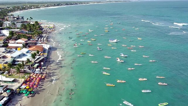 Aerial view of Enseadinha Beach in Porto de Galinhas, Pernambuco, Brazil. A bustling tropical paradise with turquoise waters, jangada boats, and tourists enjoying their summer vacation.