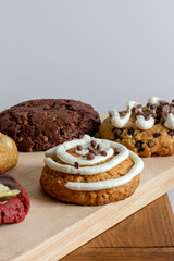 Some cookie desserts decorated with white cream and chocolate confetti on a wooden board, light gray background, space for text, vertical image
