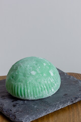 Mochi dessert green on black stone stand, wooden tabletop, space for text, light gray background, vertical image