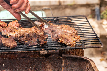 An experienced chef uses metal tongs to lift a perfectly cooked, large bone-in beef steak from a hot barbecue grill. A dynamic action shot capturing the final moment of grilling a gourmet meal.