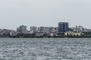 Obraz premium Grado, Italy - July 24, 2025: Panoramic view of Grado from Barbana island, with modern buildings rising above the lagoon on a cloudy day over calm northern waters.