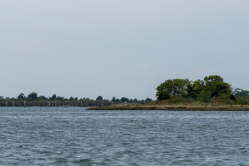 Grado, Italy - July 24, 2025: View from Barbana island over the calm lagoon waters, with a quiet stretch of land and trees under a soft overcast sky in northern Italy.
