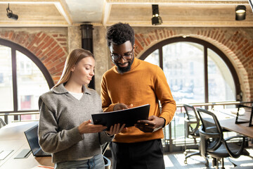 Happy young professionals reviewing report together in stylish office interior