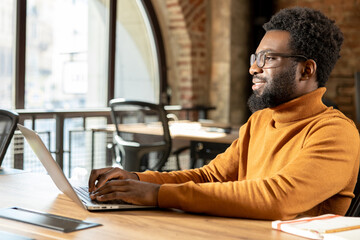 African American male professional working remotely using laptop in bright coworking space