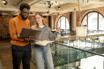 Happy young professionals reviewing report together in stylish office interior