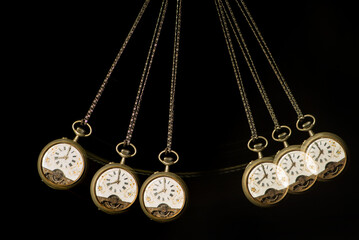 Antique pocket watch moving on a pendulum creating the illusion of multiple clocks, black background, selective focus.