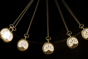 Antique pocket watch moving on a pendulum creating the illusion of multiple clocks, black background, selective focus.