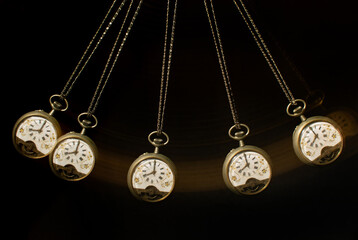 Antique pocket watch moving on a pendulum creating the illusion of multiple clocks, black background, selective focus.