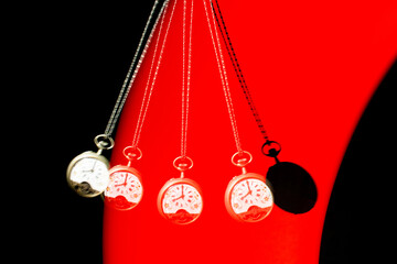 Antique pocket watch moving on a pendulum creating the illusion of multiple clocks, red-lit background, selective focus.