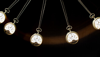 Antique pocket watch moving on a pendulum creating the illusion of multiple clocks, black background, selective focus.