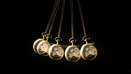 Antique pocket watch moving on a pendulum creating the illusion of multiple clocks, black background, selective focus.