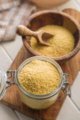 Raw couscous in jar on wooden cutting board.