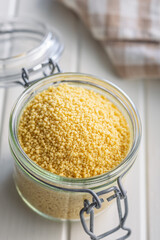 Raw couscous in jar on white table.