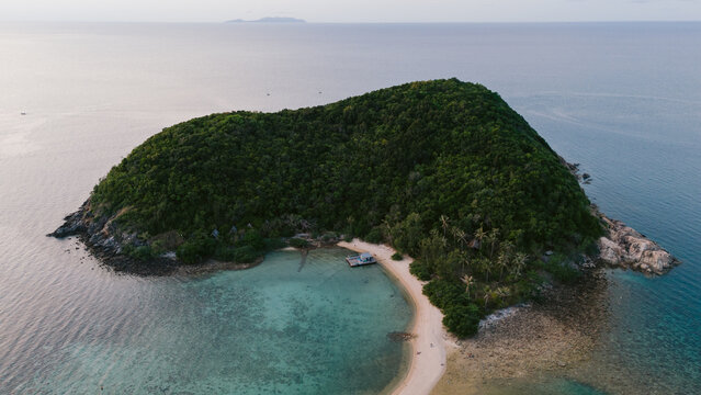 Aerial view of island lush with dense greenery meeting turquoise waters, sandy beach, and distant land, Ko Ma Beach, Surat Thani, Thailand.
