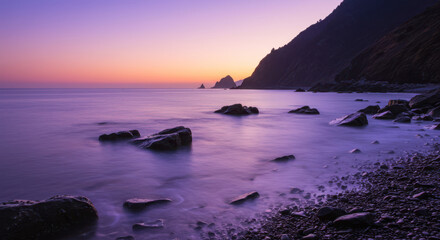 Serene purple sunset over a rocky coastline with calm ocean waters
