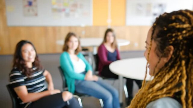 Group of young women in casual attire engaged in a discussion, likely in an indoor setting with round tables