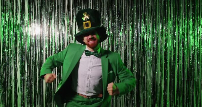 Happy funny man dressed in green costume and leprechaun hat, having fun and dancing carefree during St Patricks Day, posing against shiny background. Irish culture. Party time and celebration