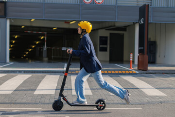 Young woman rides electric scooter on urban street wearing helmet
