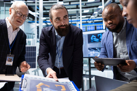 Businesspeople in production plant brainstorming. Investors and factory management colleagues looking over research and development data on paperwork, analyzing innovative manufacturing strategies