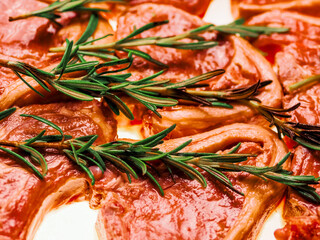 Premium quality marinated lamb loin chops and rosemary herb on white background. Uncooked raw meat on the bone in red color water based marinade to enhance dish taste.