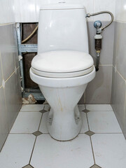 Small narrow toilet room with hole cut in wall to access and replace damaged old cast iron pipes with new modern plastic tubes. There is water filter and used water counter. Water leak repair.